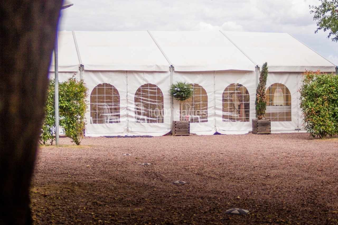 Location salle Reyrieux (Ain) - Le Clos Talançonnais #27 Grande tente blanche avec fenêtres transparentes, installée sur un sol gravillonné entouré de verdure.