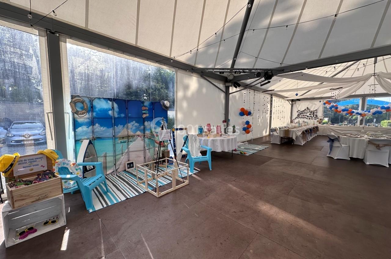 Salle décorée pour un événement avec tables dressées, ballons colorés et un espace thématique plage.