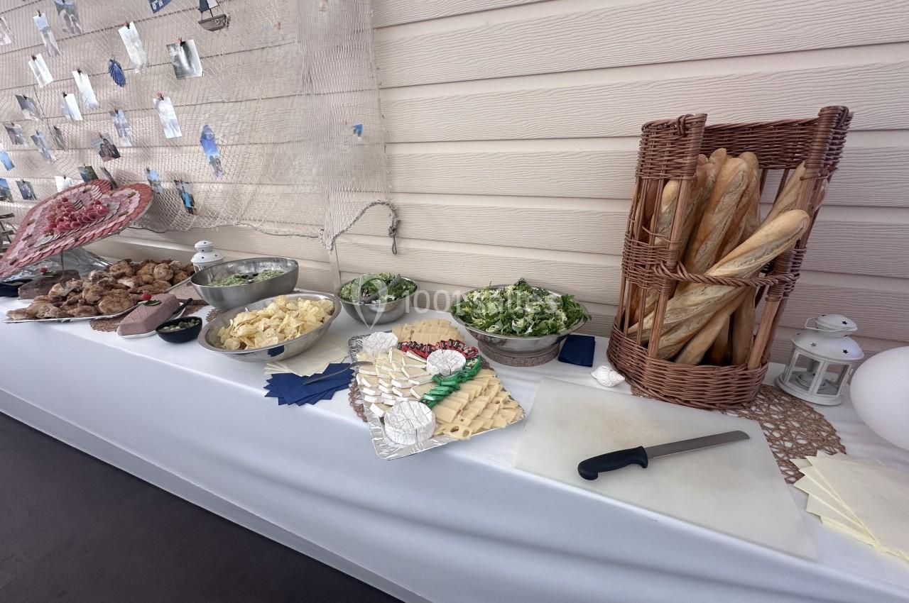 Buffet avec pain, salades, charcuterie, fromages et décor marin sur une table blanche.