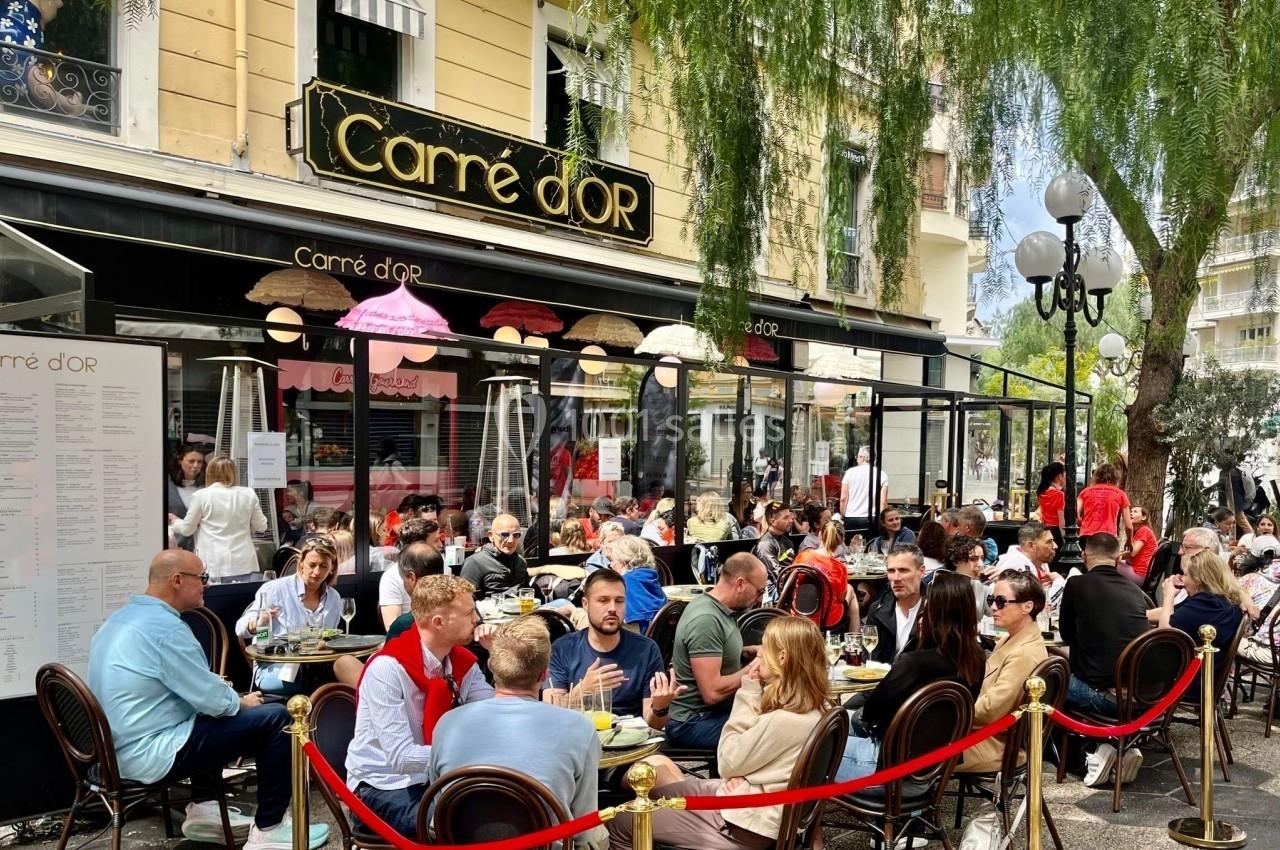 Terrasse animée d'un restaurant avec des clients attablés, entourée de végétation et d'une enseigne ’Carré d'Or’.