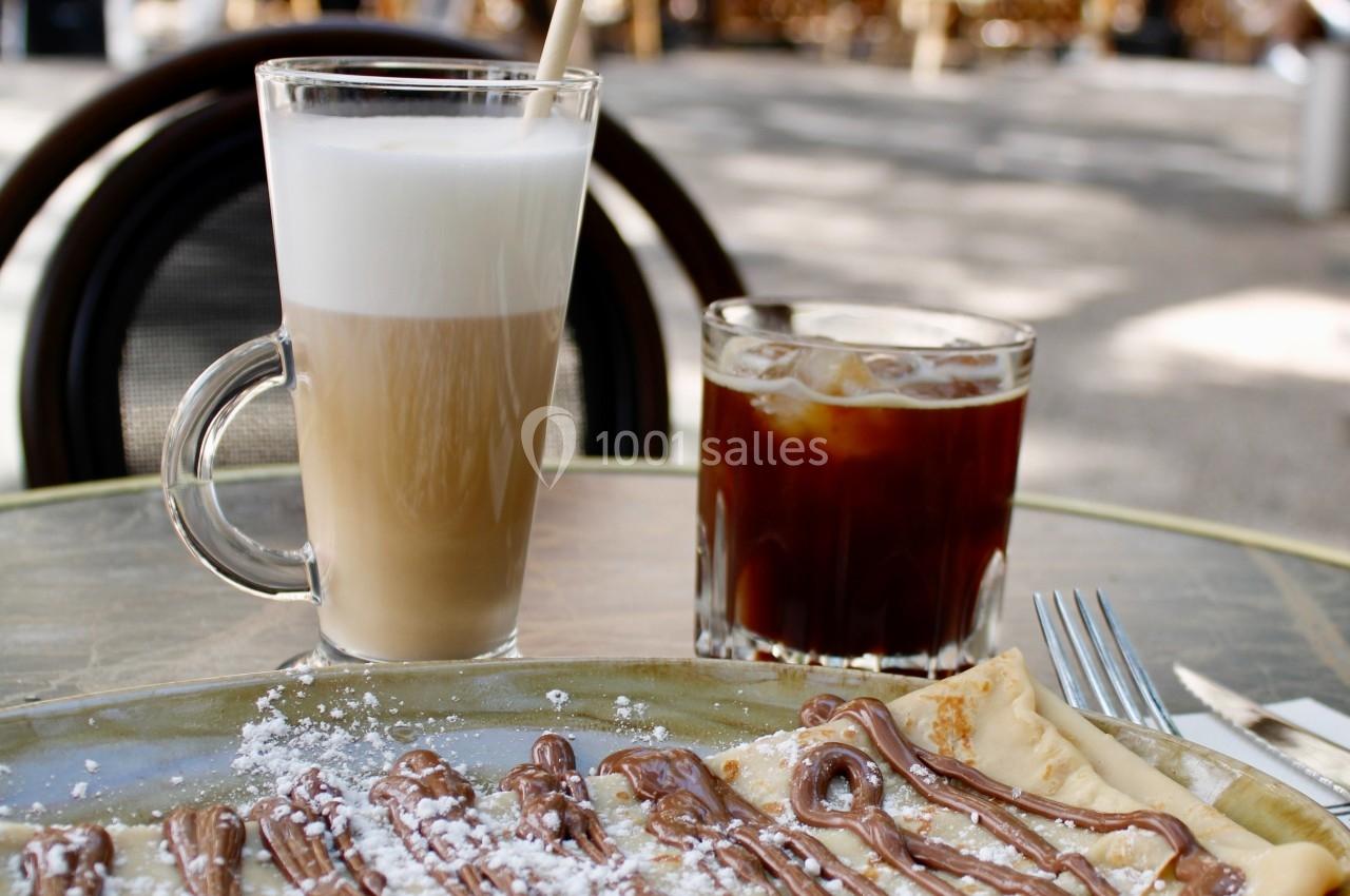 Crêpe garnie de chocolat avec un latte et un café glacé sur une table en terrasse, arrière-plan flou de café animé.