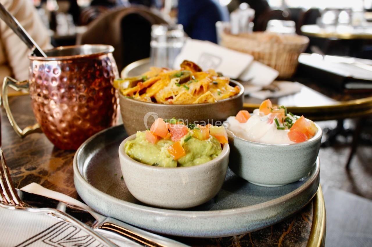 Assiette avec guacamole, crème fraîche, nachos et une boisson dans un cadre de restaurant.