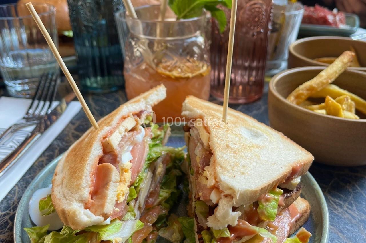 Sandwich club garni de salade, tomate et poulet, servi avec des frites et une boisson sur une table de restaurant.
