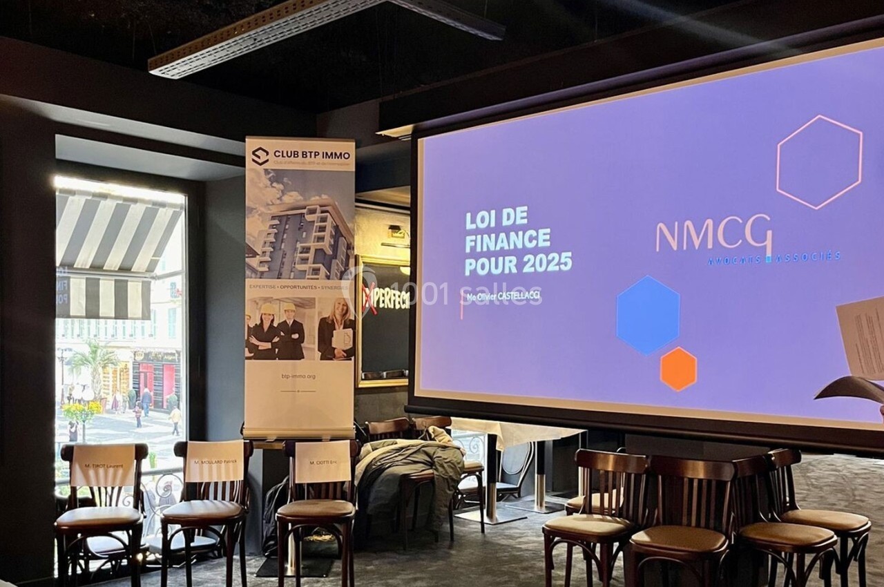 Salle de conférence avec un écran affichant ’Loi de finance pour 2025’, des chaises alignées et une bannière promotionnelle.