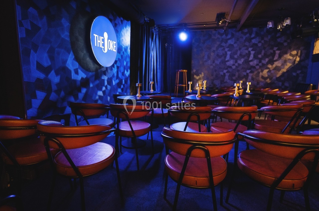 Salle de spectacle avec des chaises rouges disposées face à une scène éclairée et un mur décoré.