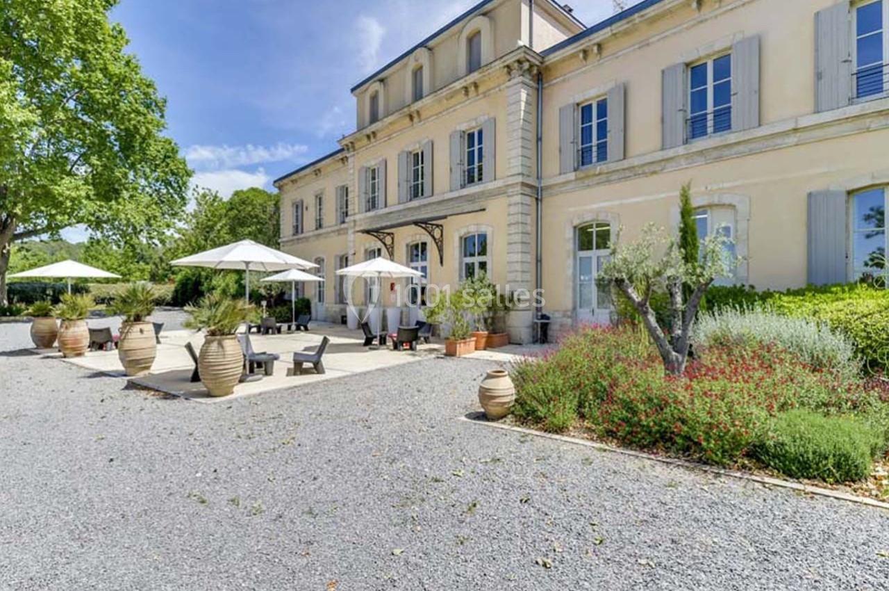 Façade d'un bâtiment ancien avec terrasse aménagée, parasols, pots décoratifs et végétation environnante.