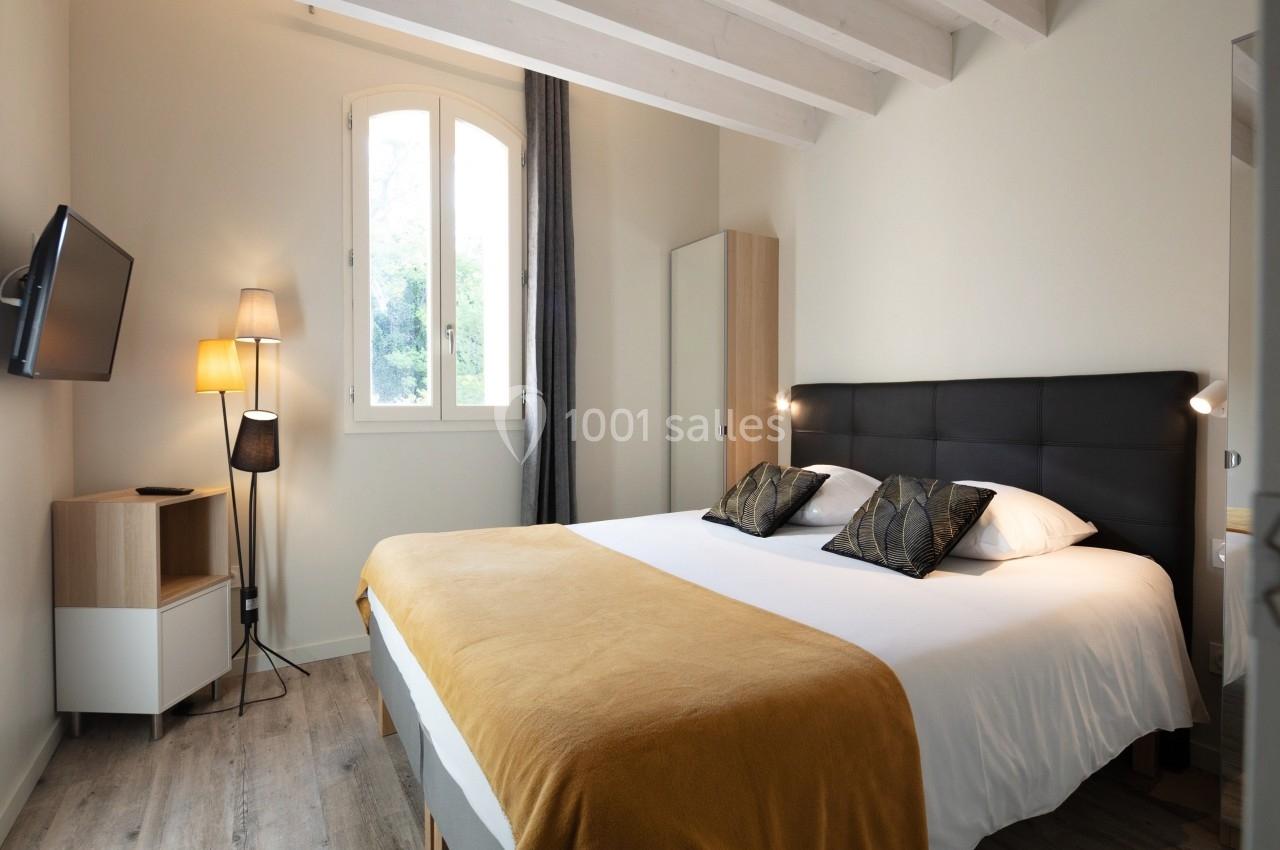 Chambre lumineuse avec lit double, couvre-lit jaune, lampe d'appoint et fenêtre donnant sur un extérieur arboré.