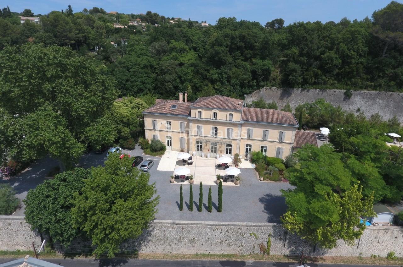 Vue aérienne d'un bâtiment ancien entouré de végétation, avec une cour aménagée et des tables en extérieur.