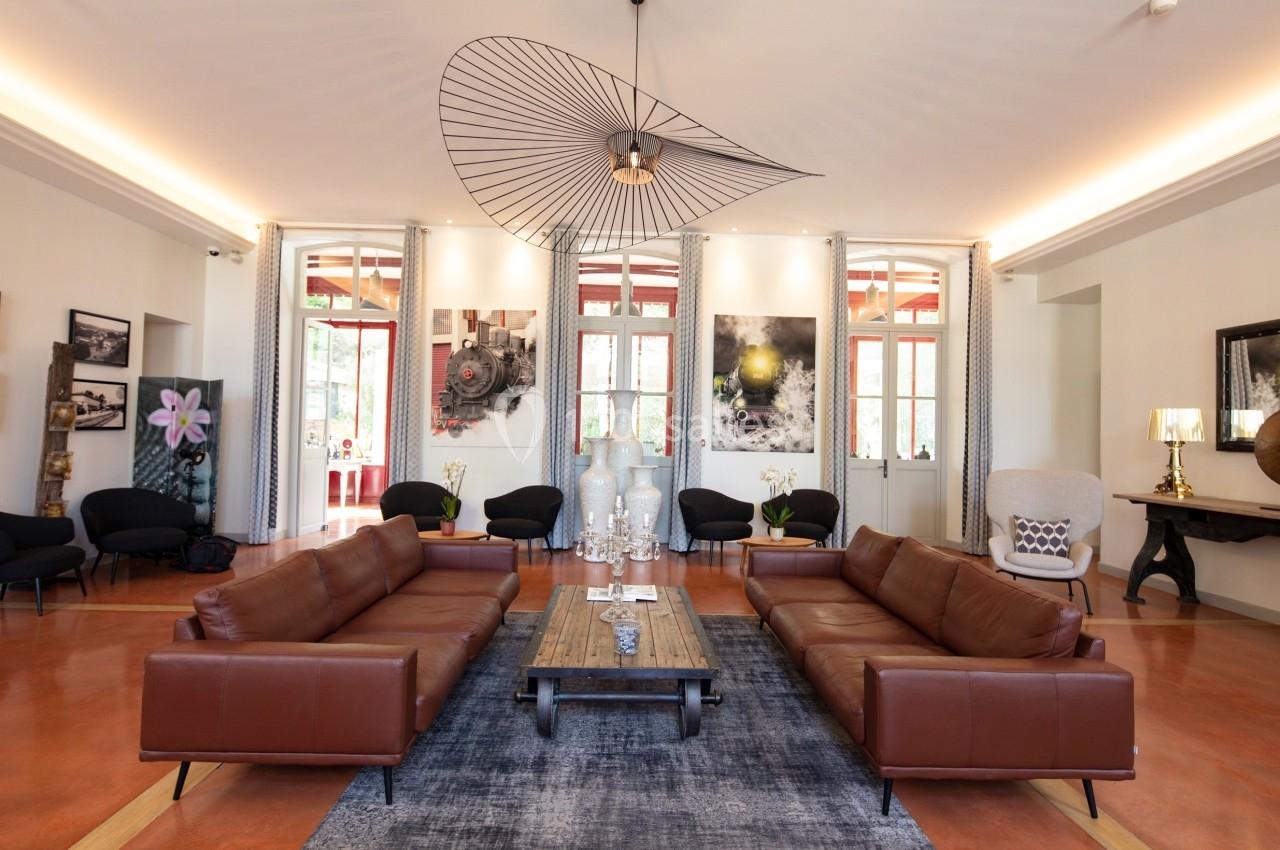 Salon spacieux avec canapés en cuir marron, table basse en bois, tapis gris et luminaire design suspendu.