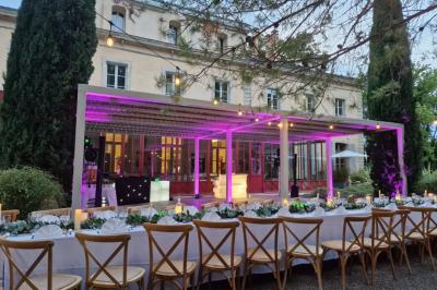Miniature Location salle Sommières (Gard) - Domaine de l’Estelou #44 Grande table dressée en extérieur avec des chaises en bois, sous une pergola illuminée de lumières violettes, devant un…