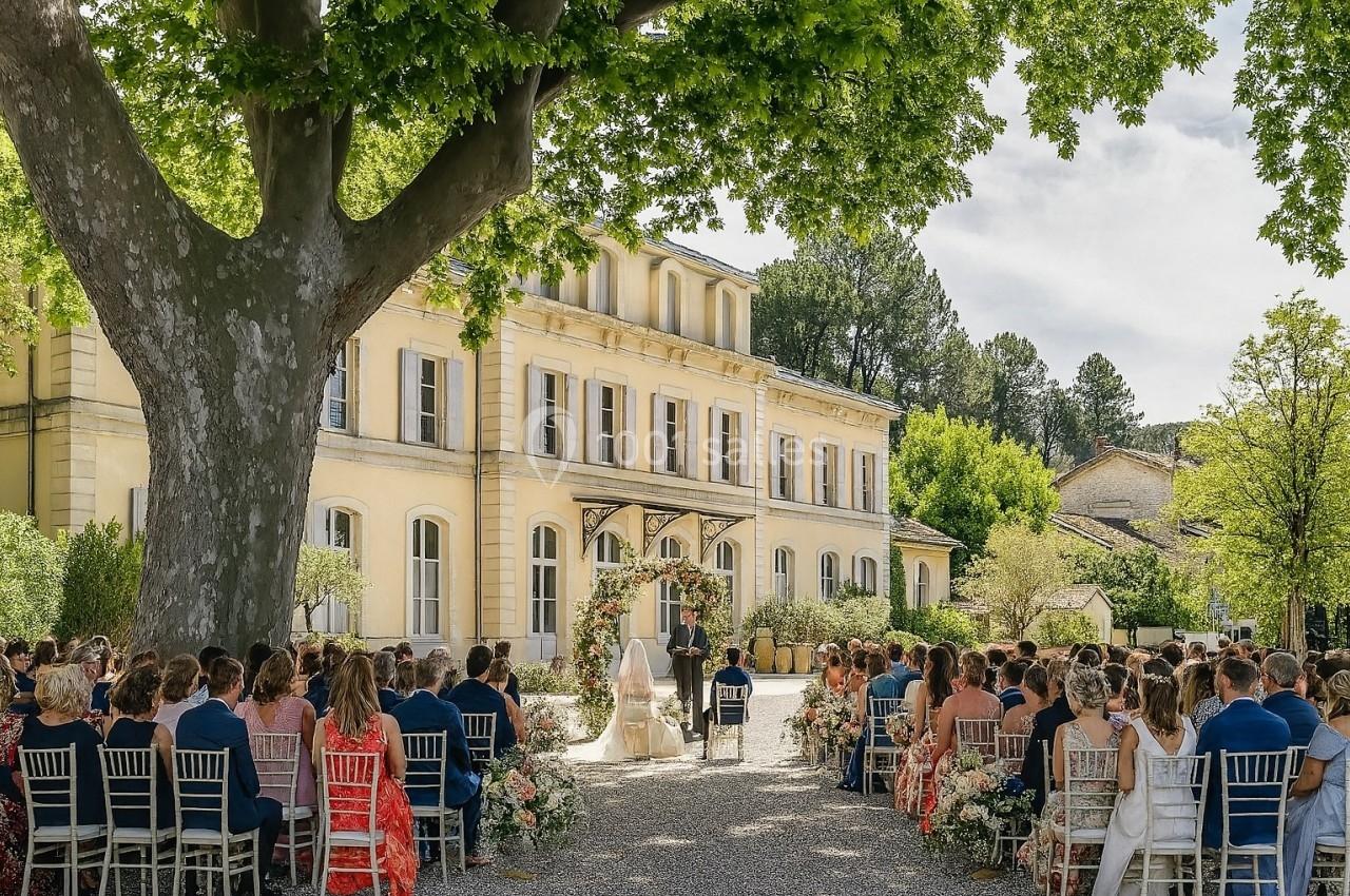 Cérémonie de mariage en plein air devant un grand bâtiment jaune, entourée d'invités assis sous un arbre.