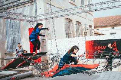 Deux acrobates exécutent une figure d'équilibre sur une caisse, devant un public dans un espace éclairé.