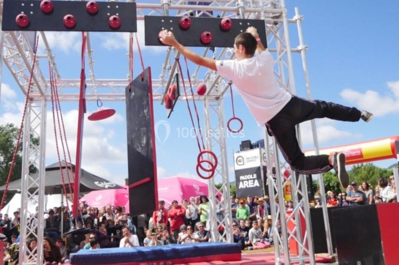 Un homme traverse un parcours d'obstacles suspendus lors d'un événement en plein air devant un public.