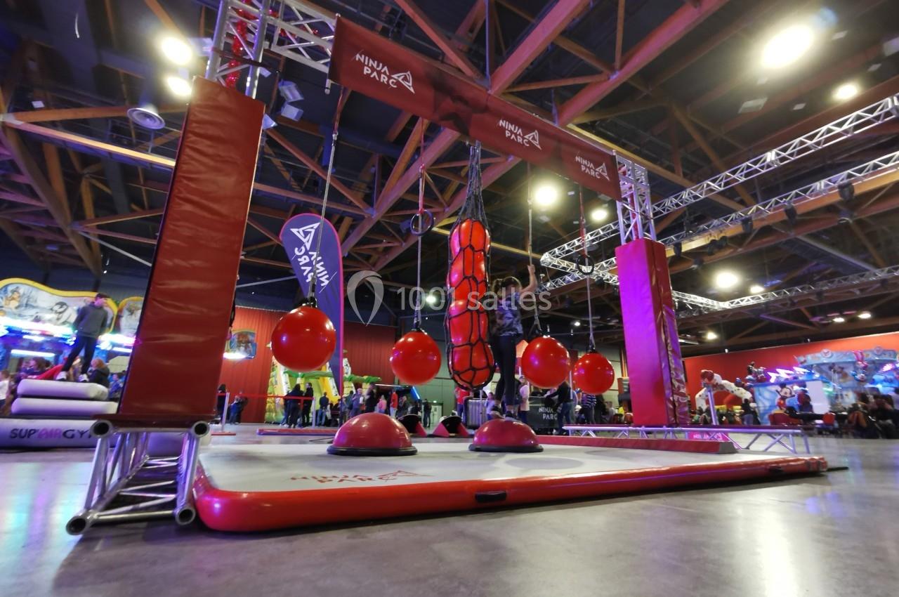 Parcours d'obstacles intérieur avec structures suspendues et ballons rouges, sous un éclairage de salle de loisirs.