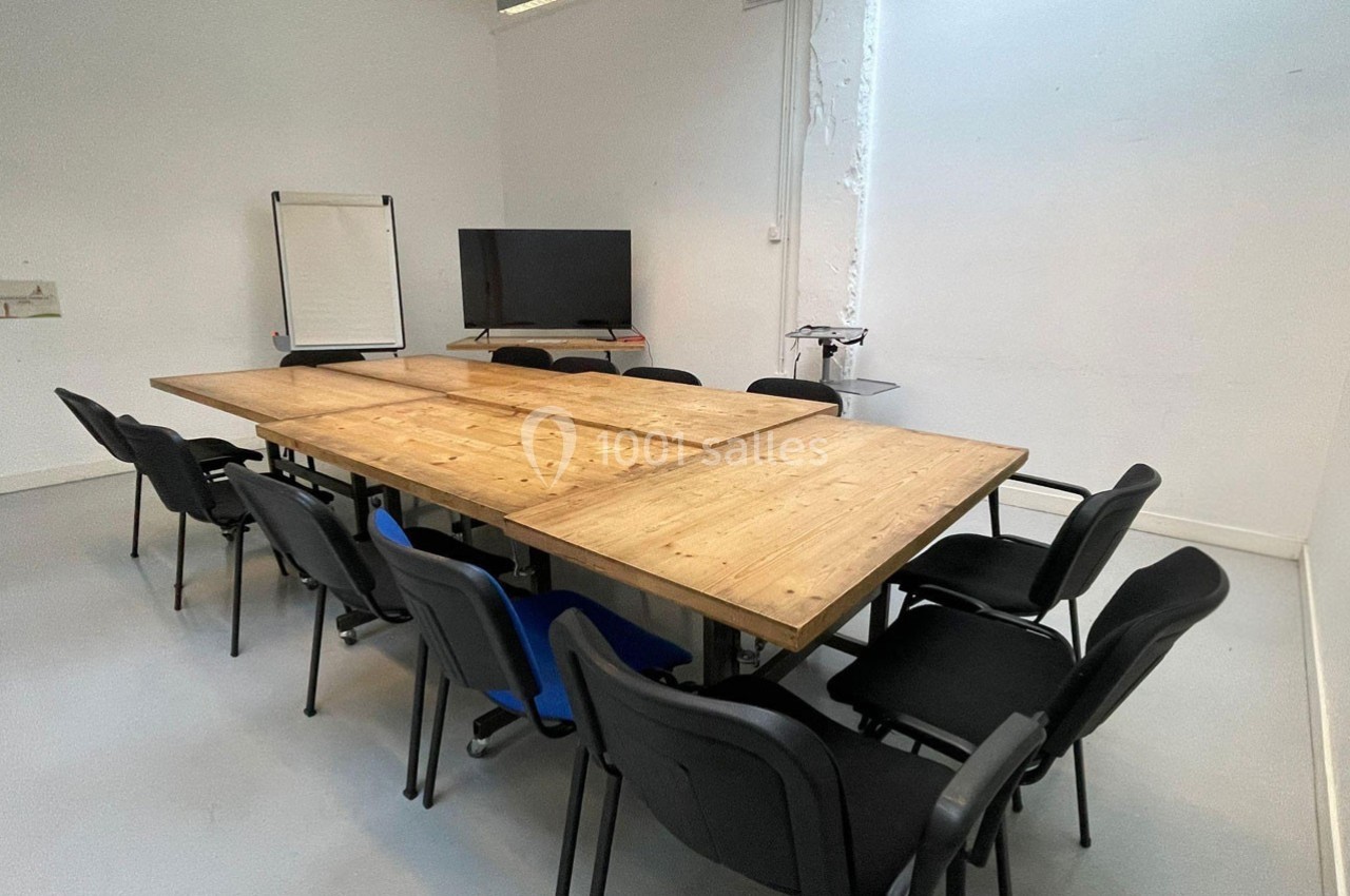 Salle de réunion avec une grande table en bois entourée de chaises noires, un écran et un tableau blanc en arrière-plan.