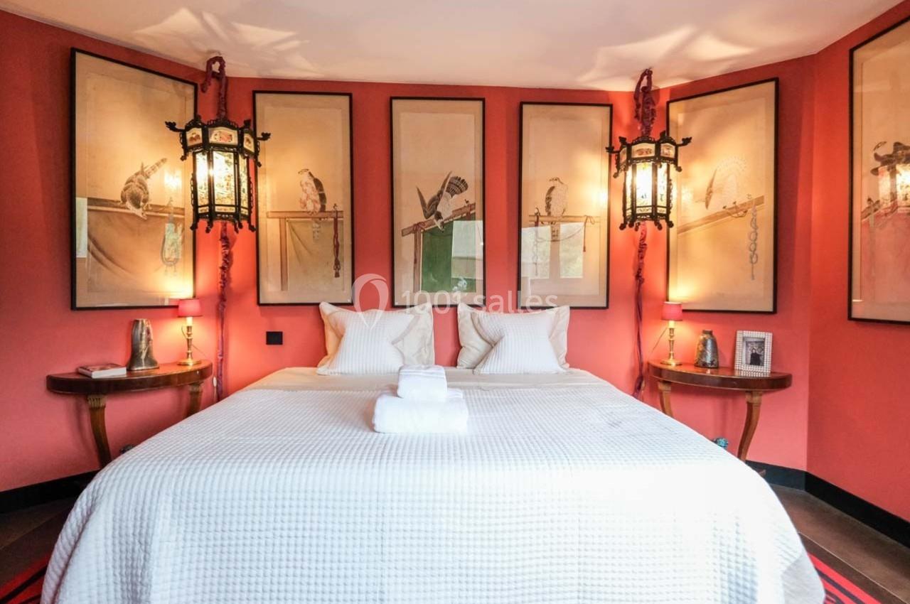 Chambre avec murs rouges, lit double avec linge blanc, lanternes suspendues et illustrations encadrées d'oiseaux.