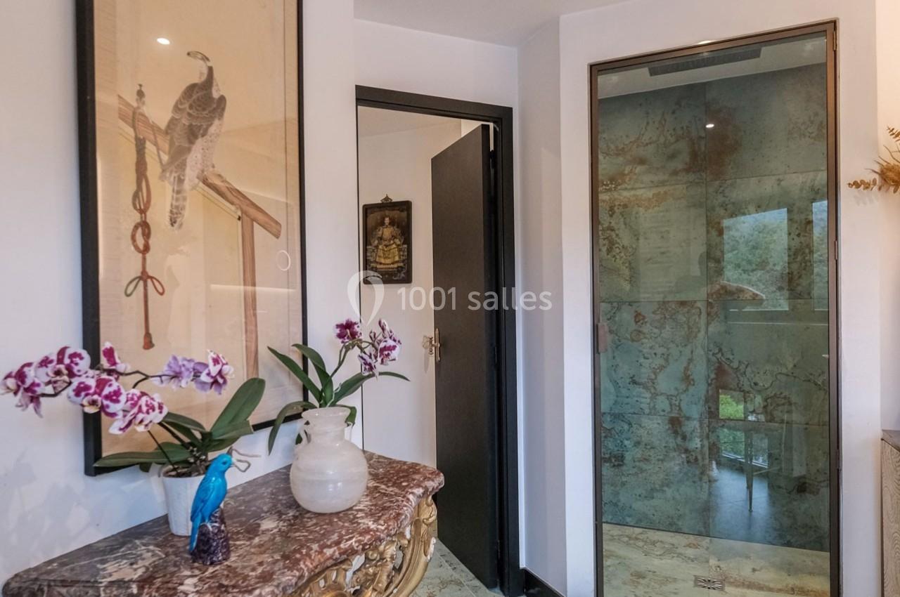 Un couloir avec une table en marbre décorée d'orchidées, un tableau mural et une porte vitrée donnant sur l'extérieur.