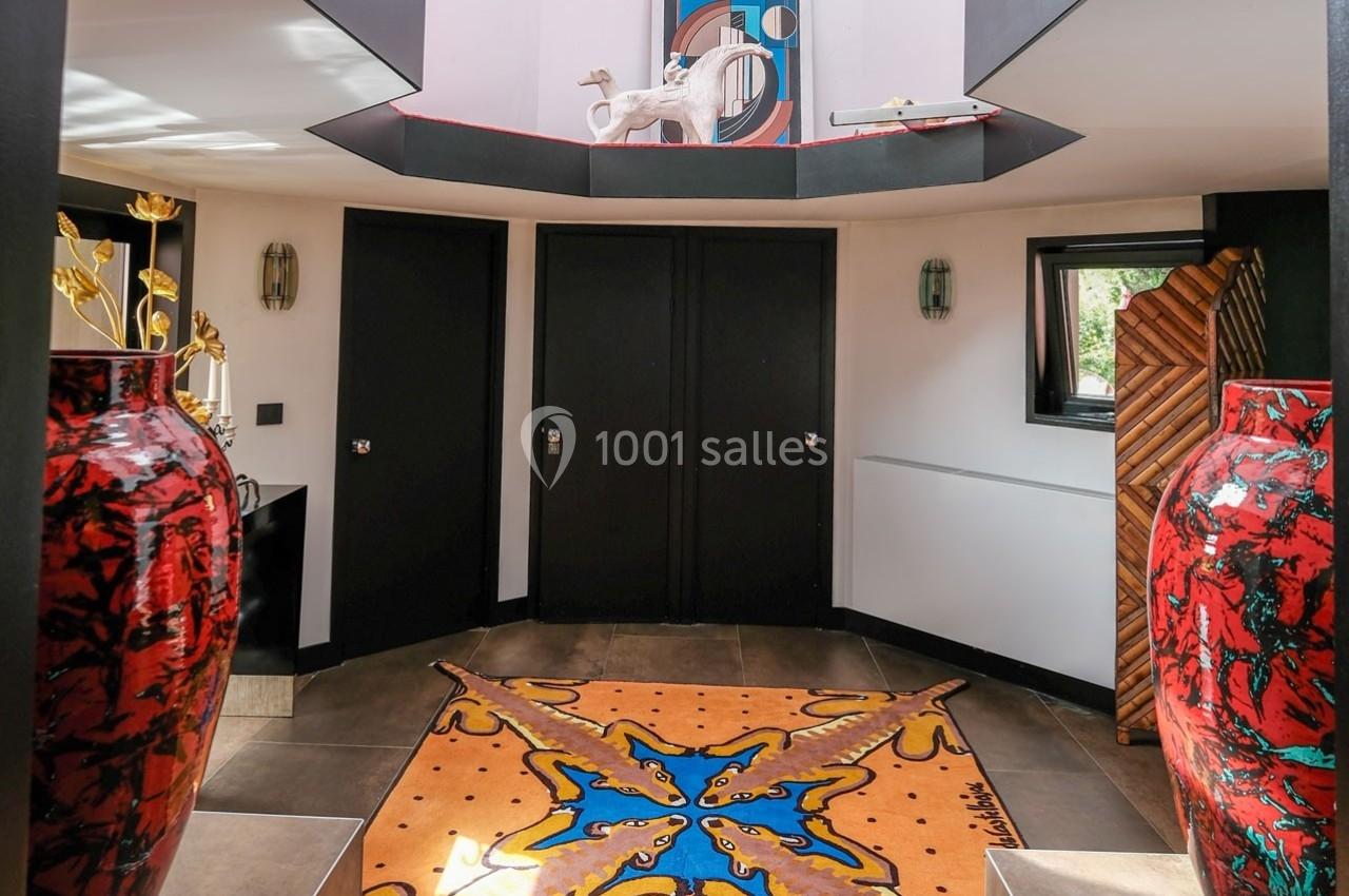 Entrée lumineuse avec tapis coloré, vases rouges décoratifs, portes noires et œuvres d'art modernes sur les murs.