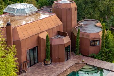Maison contemporaine en cuivre avec grandes baies vitrées, terrasses et piscine, entourée de végétation.