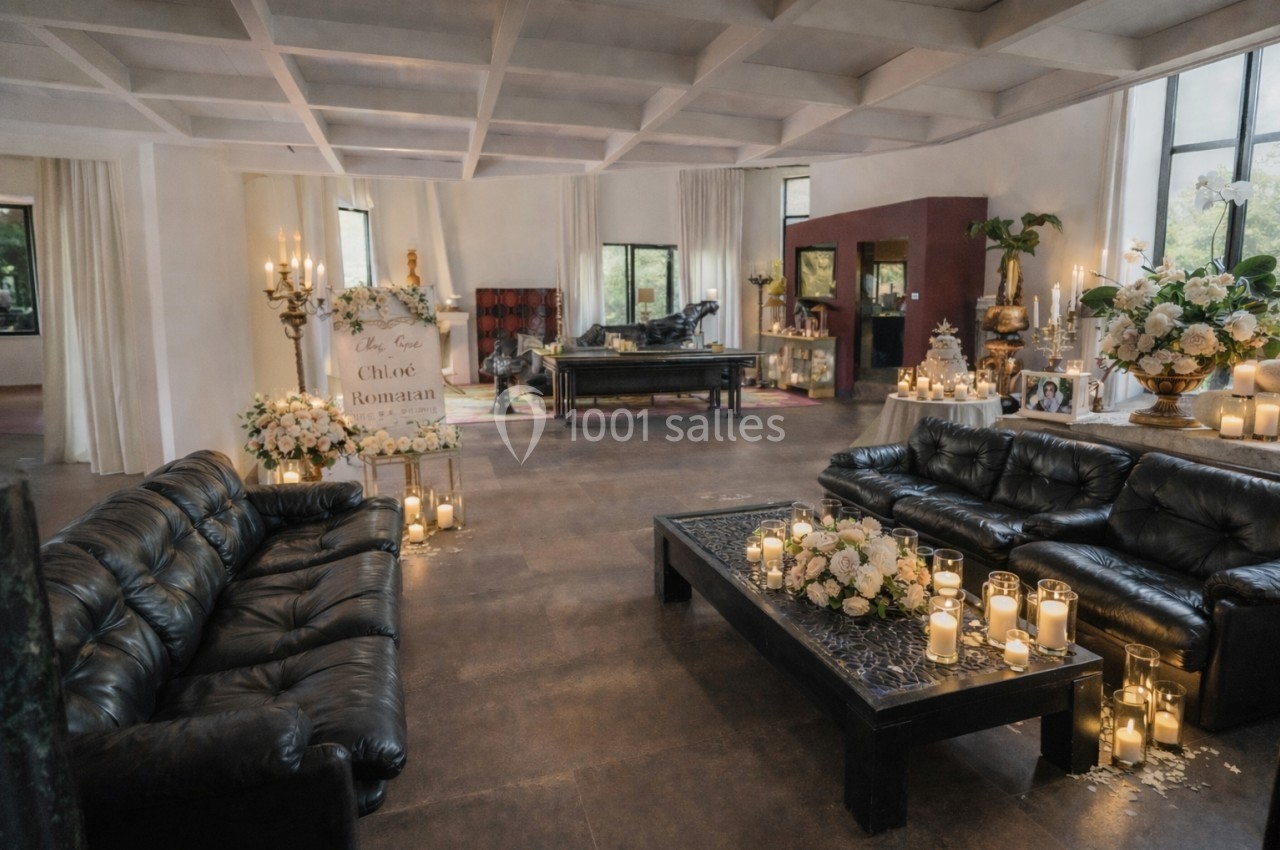 Salle décorée pour une cérémonie, avec canapés en cuir, bougies, fleurs et un panneau portant des noms.