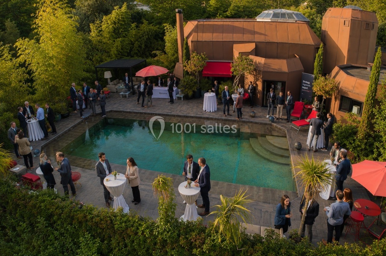 Vue aérienne d'un événement en plein air autour d'une piscine, avec des invités discutant près de tables hautes.