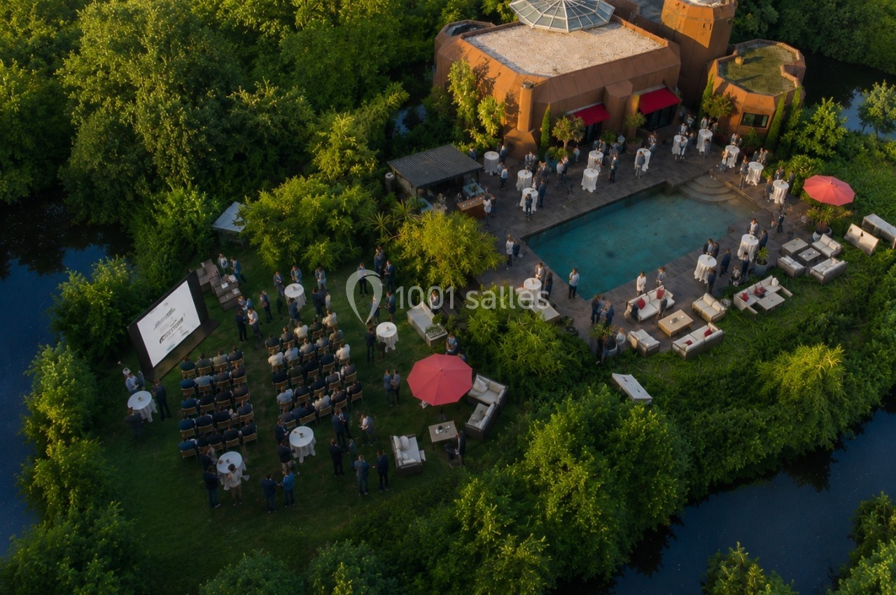 Vue aérienne d'un événement en plein air autour d'une piscine, avec des invités, des tables et une présentation sur écran.