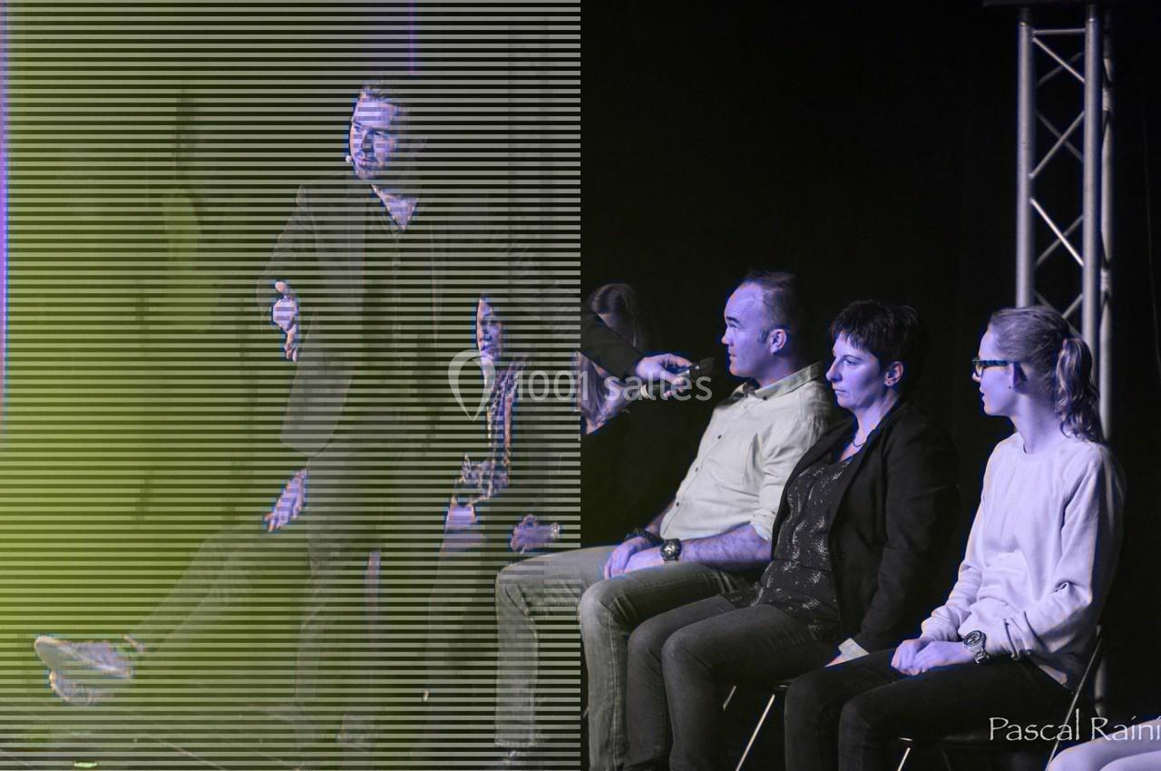 Un hypnotiseur sur scène interagit avec quatre personnes assises, sous un éclairage tamisé.