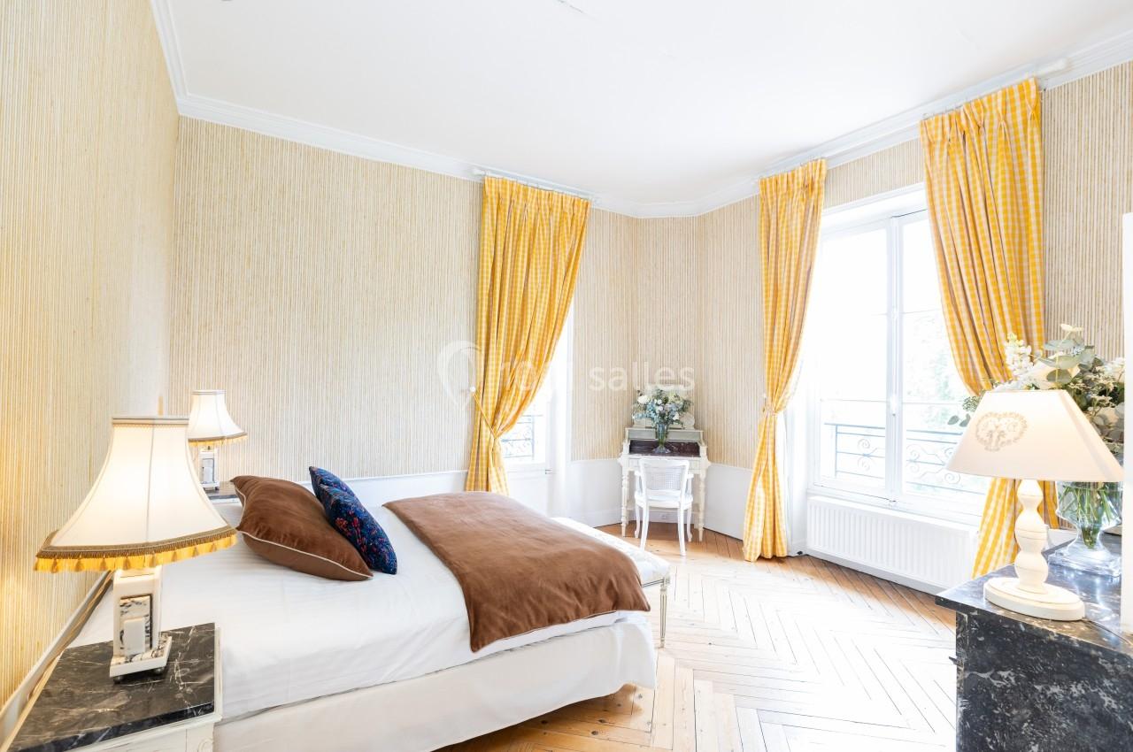 Chambre lumineuse avec lit double, parquet en bois, rideaux jaunes et bureau près d'une fenêtre.