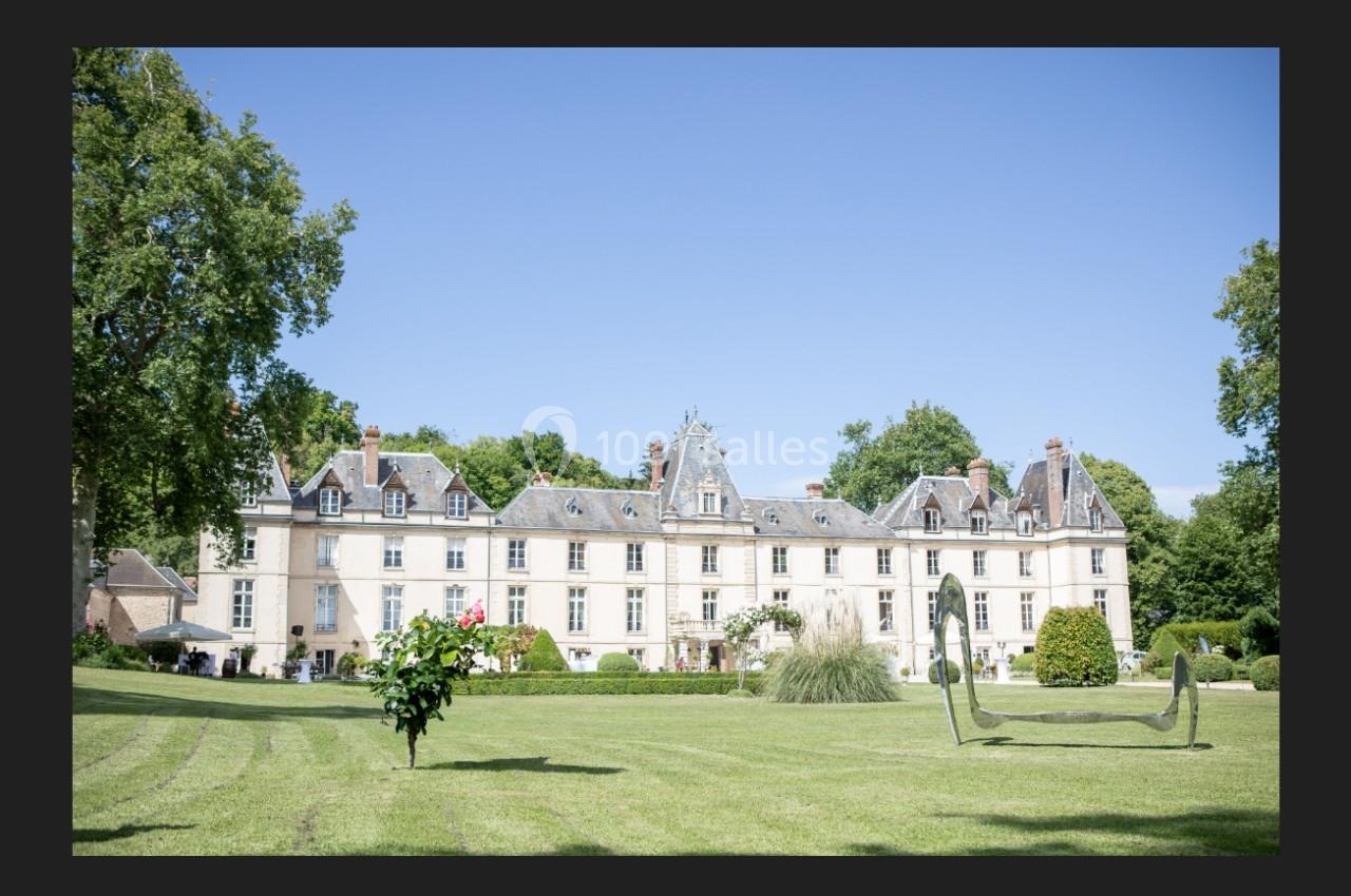 Façade d'un château entouré d'un parc verdoyant avec pelouse, arbres et sculptures modernes.