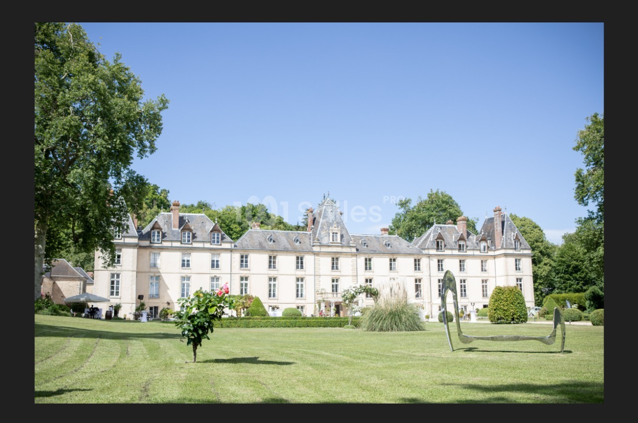 Façade d'un château entouré d'un parc verdoyant avec pelouse, arbres et sculptures modernes.