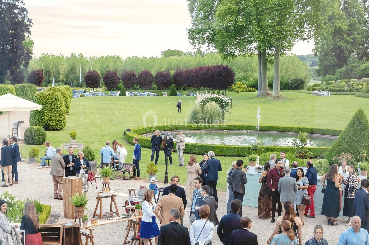 Groupe de personnes rassemblées dans un jardin avec pelouse, fontaine centrale et arbres en arrière-plan.