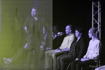 Un homme sur scène interagit avec quatre personnes assises, éclairées par une lumière contrastée.