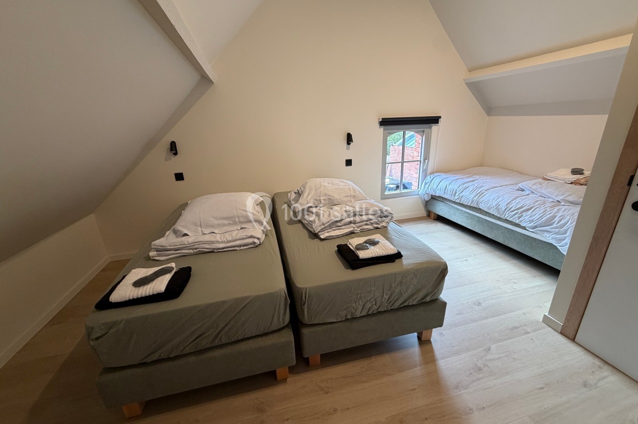 Chambre mansardée avec deux lits simples côte à côte, un lit double en arrière-plan et une fenêtre donnant sur l'extérieur.
