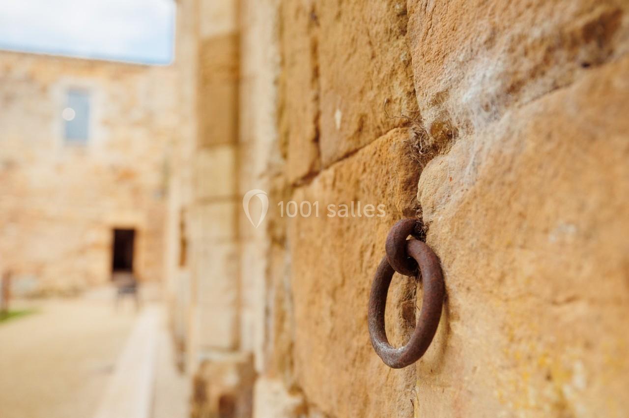 Anneau métallique fixé à un mur en pierre ancienne, avec une allée pavée visible en arrière-plan.