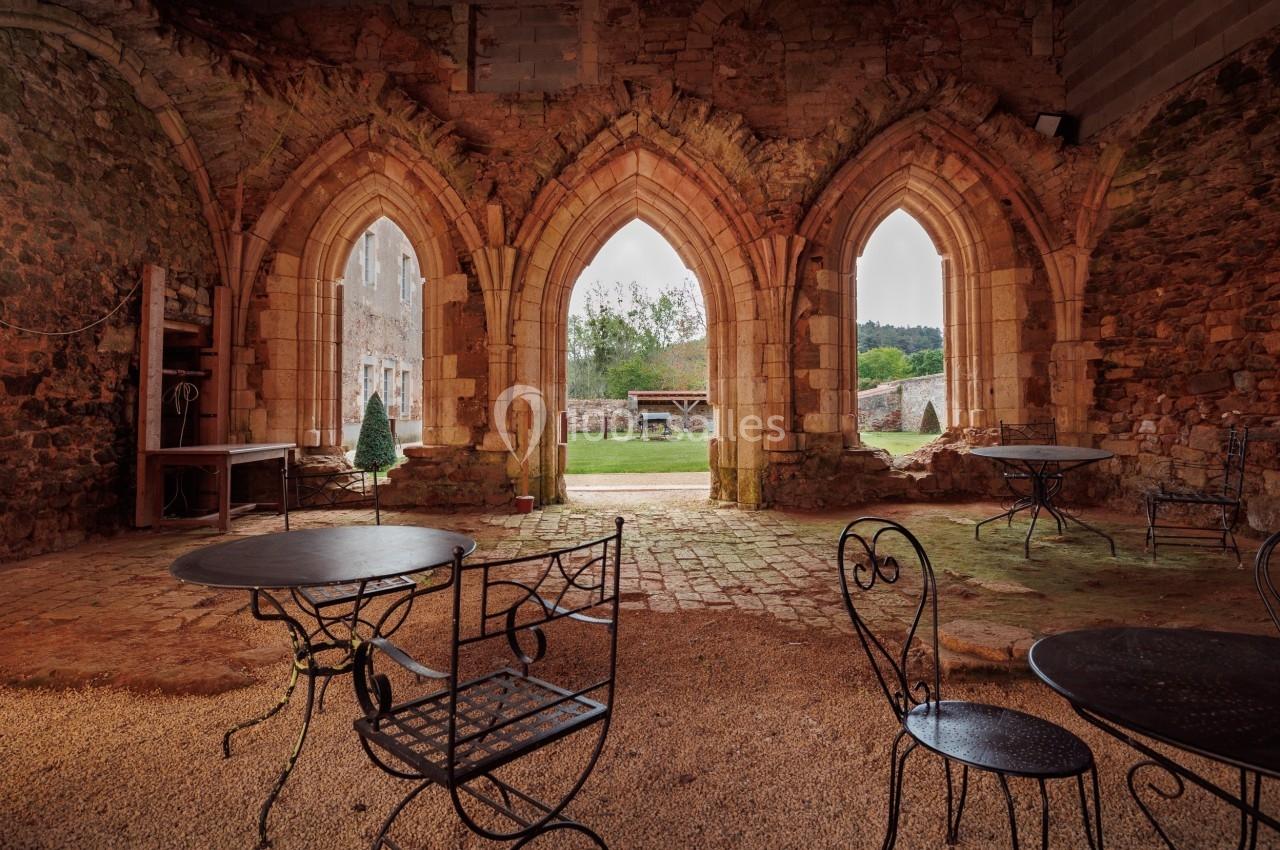 Vue intérieure d'une ancienne bâtisse en pierre avec des arches ouvertes donnant sur une cour verdoyante.