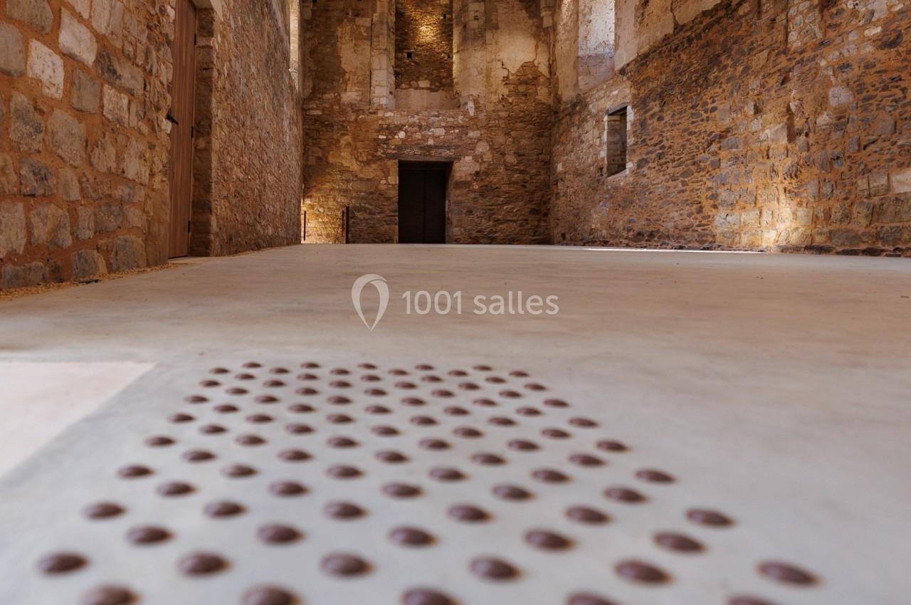 Intérieur d'un bâtiment en pierre avec un sol tactile pour guider les personnes malvoyantes vers une porte au fond.