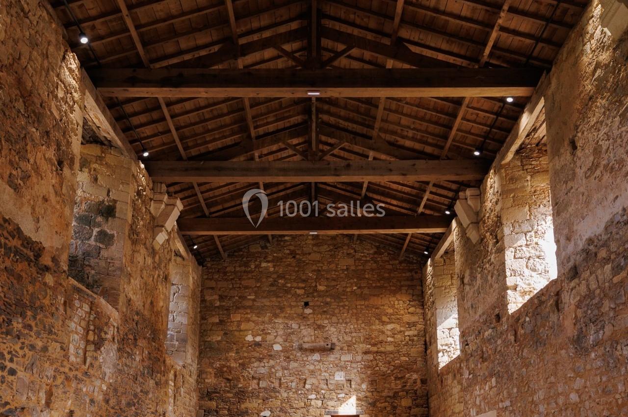 Intérieur d'un bâtiment en pierre avec un plafond en bois, éclairé par des ouvertures laissant entrer la lumière naturelle.