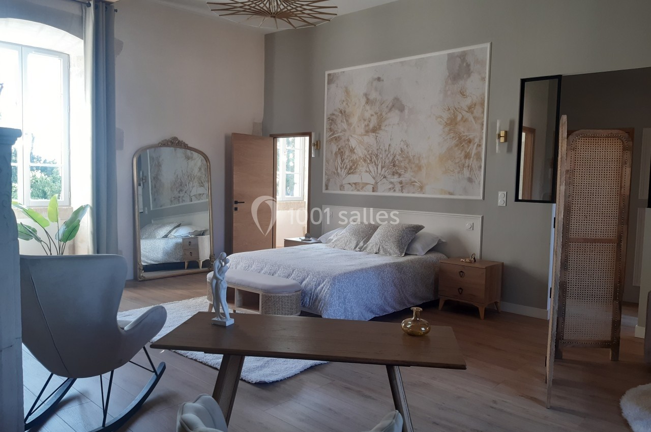 Chambre lumineuse avec lit double, bureau en bois, miroir sur pied, paravent en rotin et décoration murale.