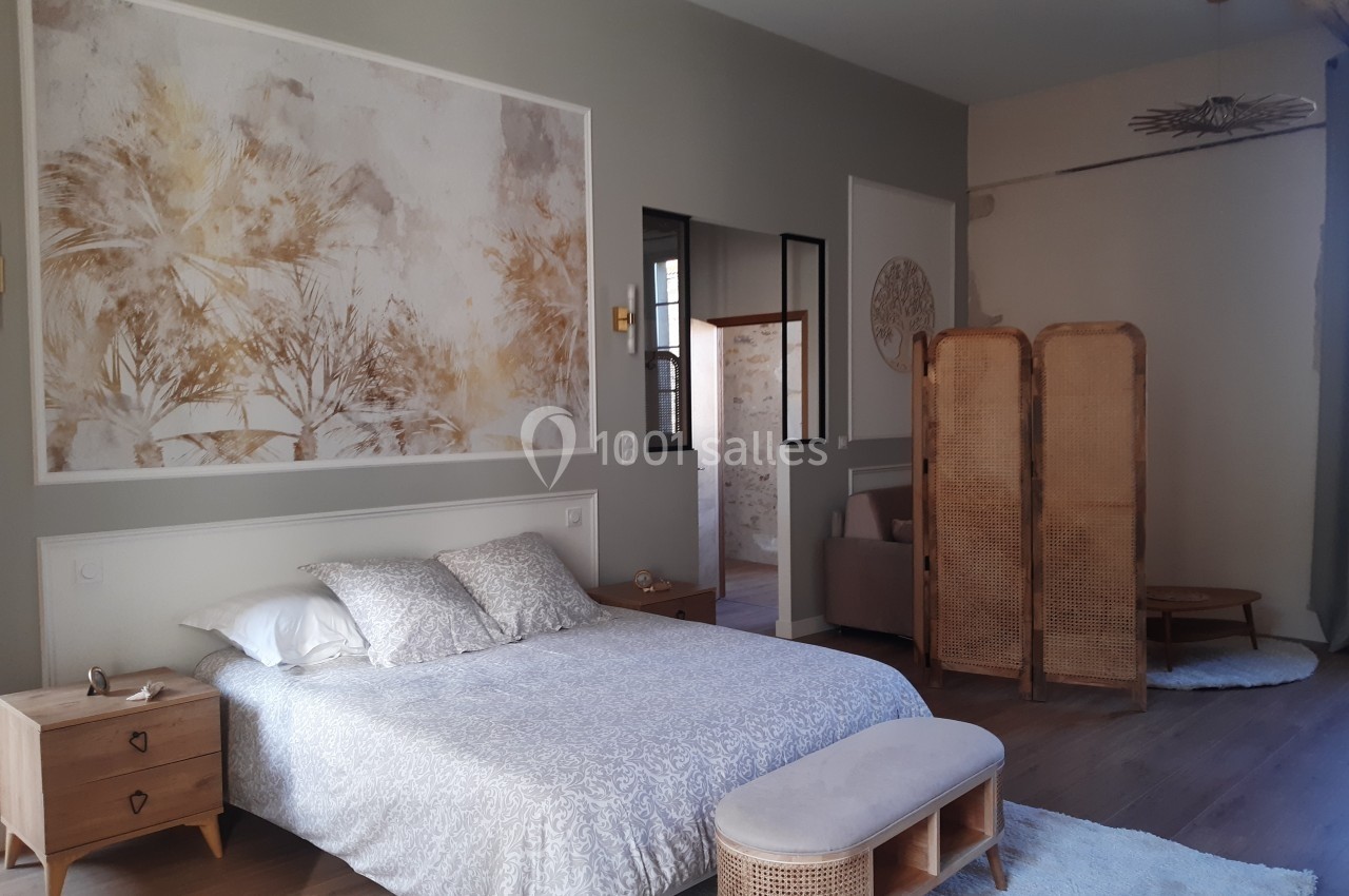 Chambre lumineuse avec lit double, paravent en rotin, décoration murale végétale et mobilier en bois clair.