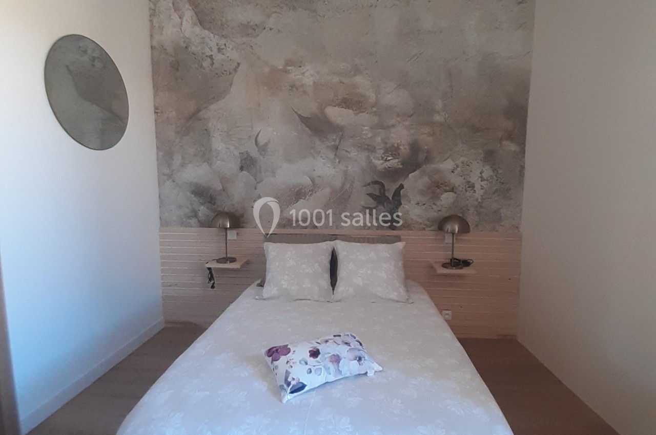 Chambre avec un lit double, tête de lit en bois clair, mur décoré d'une fresque florale et éclairage mural discret.
