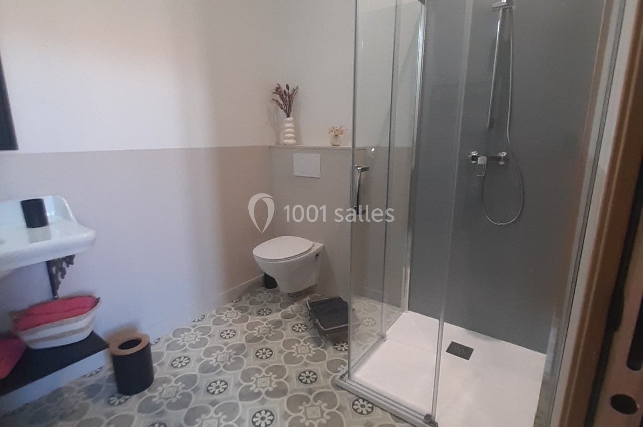 Salle de bain avec douche vitrée, lavabo, toilettes suspendues et sol en carreaux à motifs géométriques.