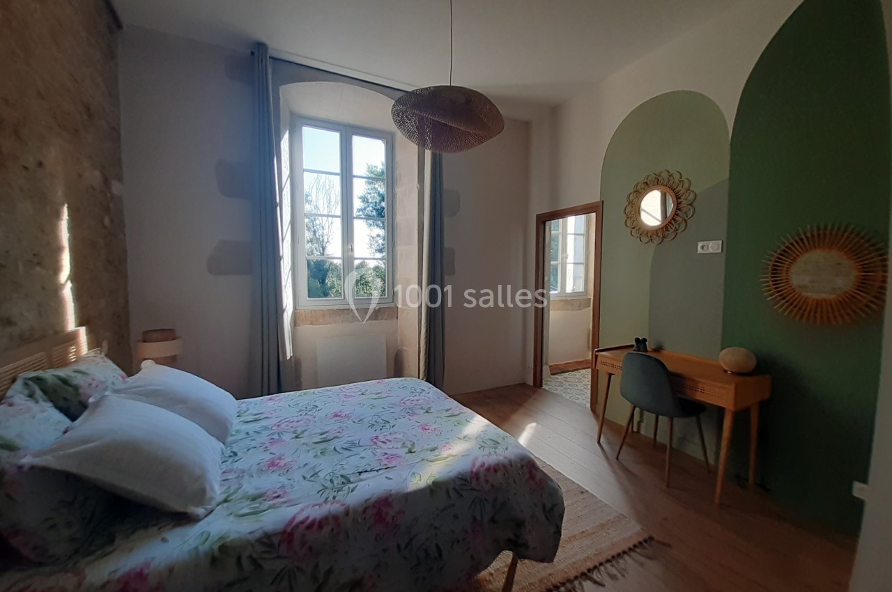 Chambre lumineuse avec lit double, bureau en bois, miroir rond et mur partiellement peint en vert.
