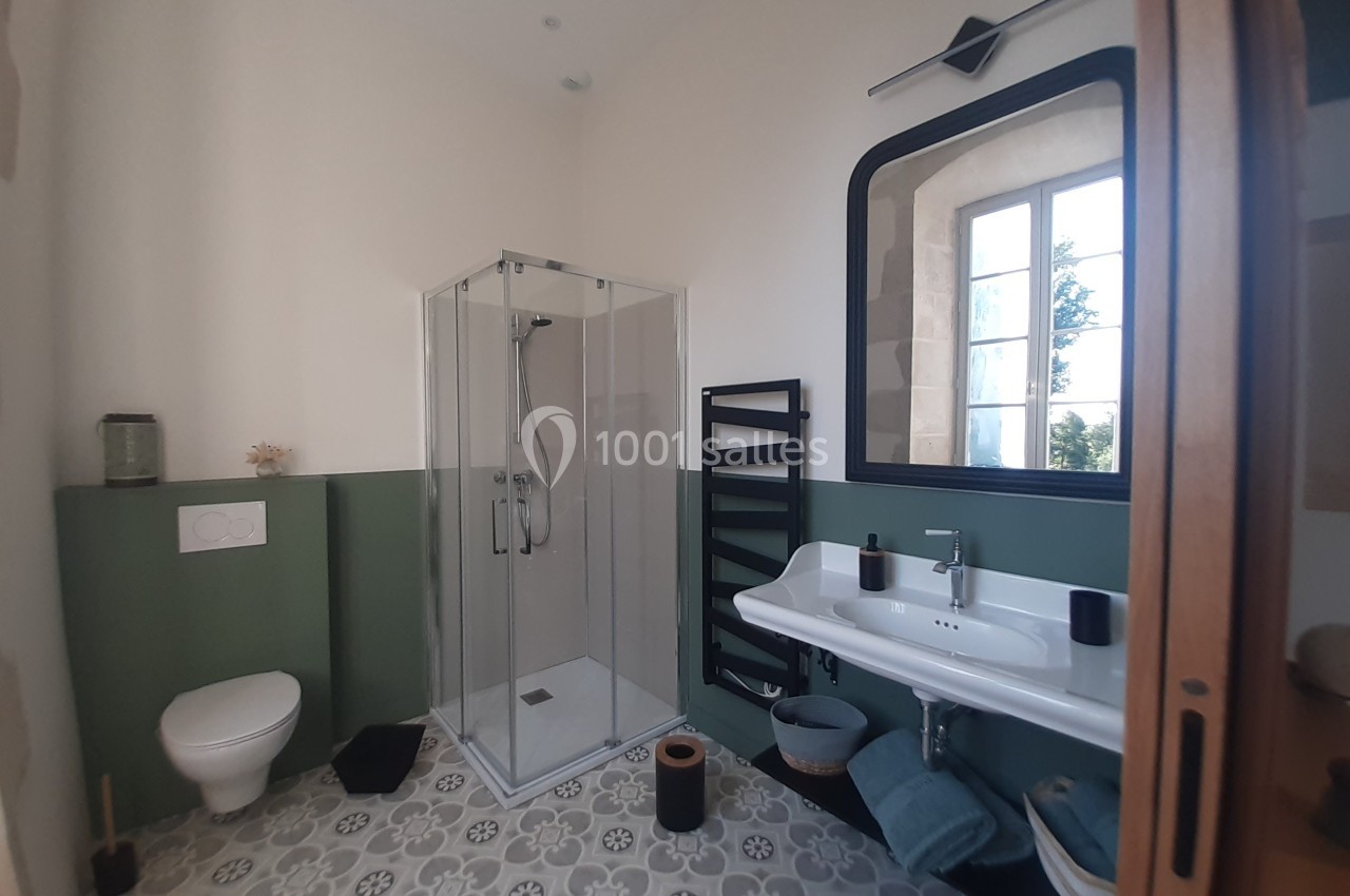 Salle de bain lumineuse avec douche vitrée, lavabo double, toilettes et décoration moderne sur un sol à motifs.