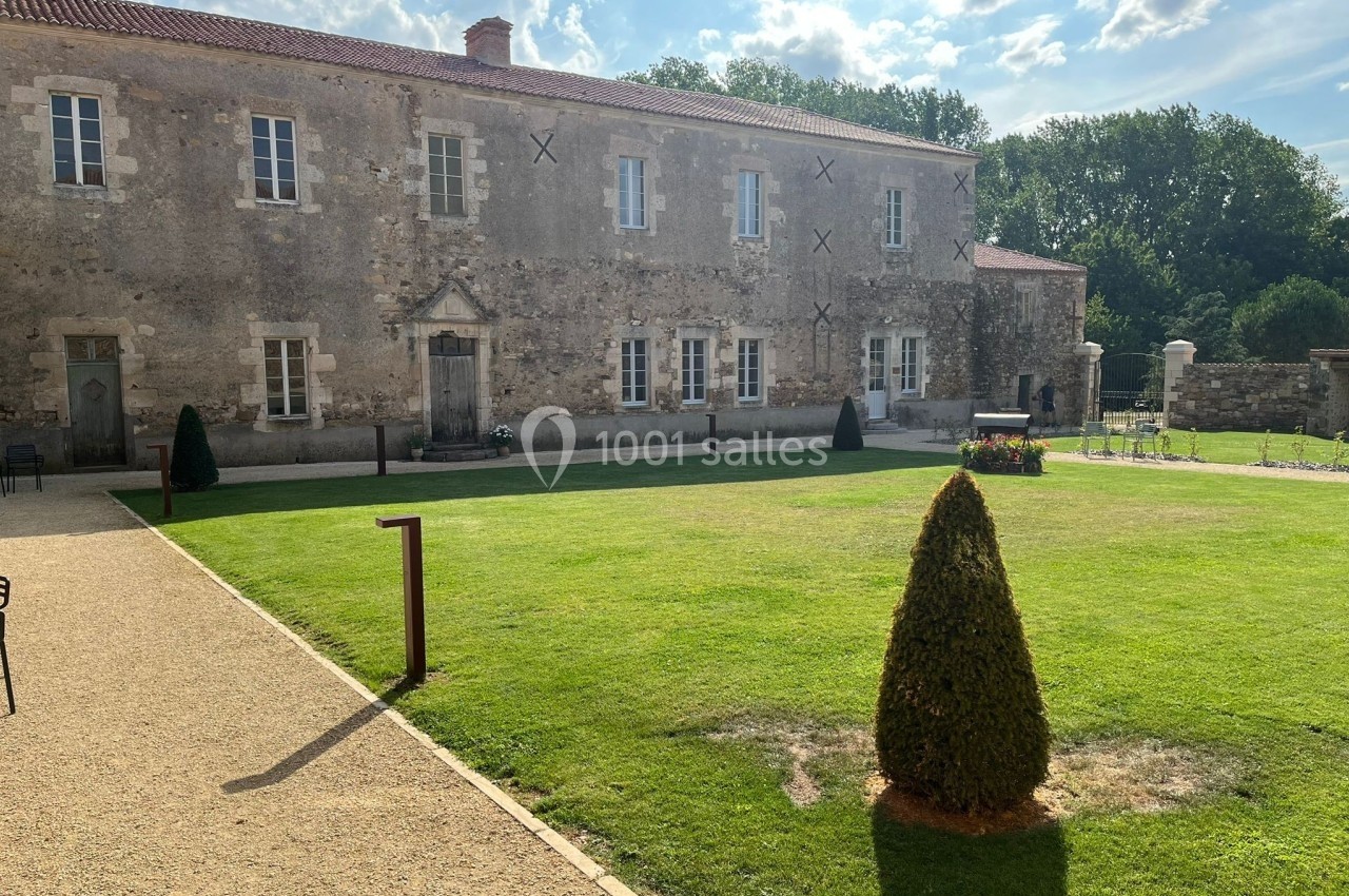 Façade d'un bâtiment en pierre entouré d'une pelouse bien entretenue et d'allées gravillonnées, sous un ciel partiellement…