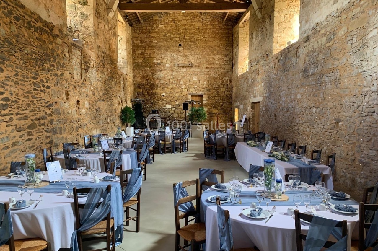 Salle en pierre avec tables rondes dressées pour un événement, nappes blanches et décorations grises.