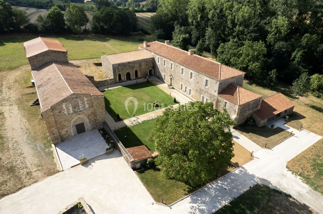 Vue aérienne d'un domaine rural avec bâtiments en pierre, toits en tuiles et cour centrale arborée.