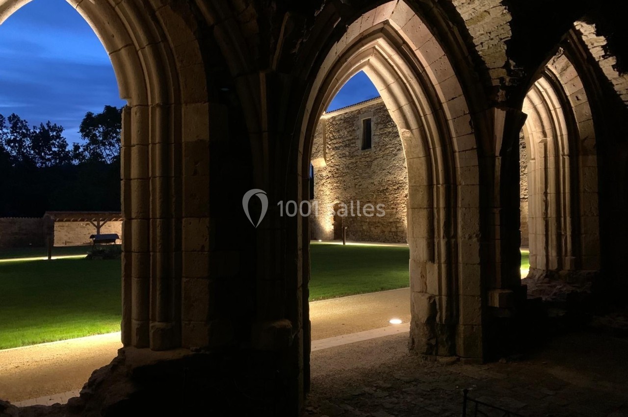 Vue nocturne d'arches en pierre éclairées, donnant sur une cour avec pelouse et murs en pierre.