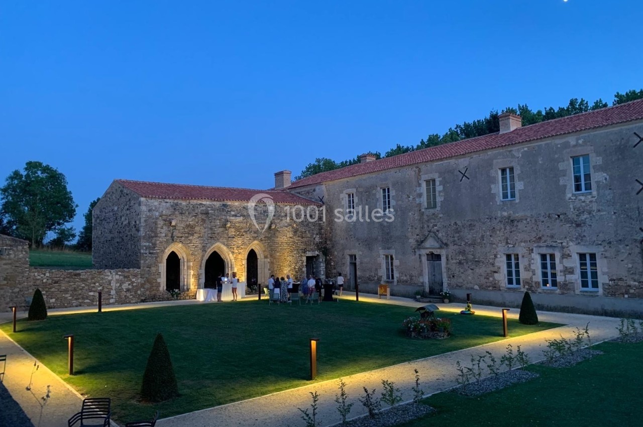 Cour intérieure d'un bâtiment historique en pierre, éclairée en soirée avec des invités rassemblés près d'une arche.