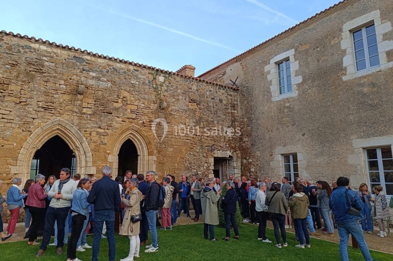 Groupe de personnes rassemblées dans une cour extérieure, près d'un bâtiment en pierre ancienne avec des arches.