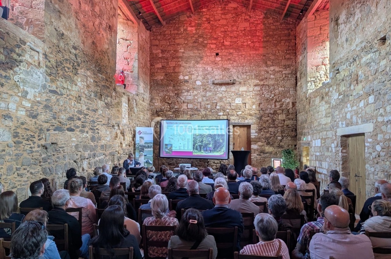 Un groupe de personnes assiste à une présentation dans une salle en pierre avec un écran de projection.